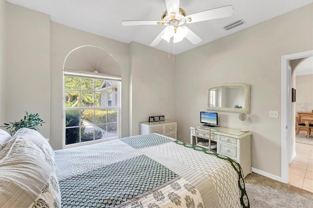 carpeted bedroom with arched walkways, baseboards, visible vents, and ceiling fan