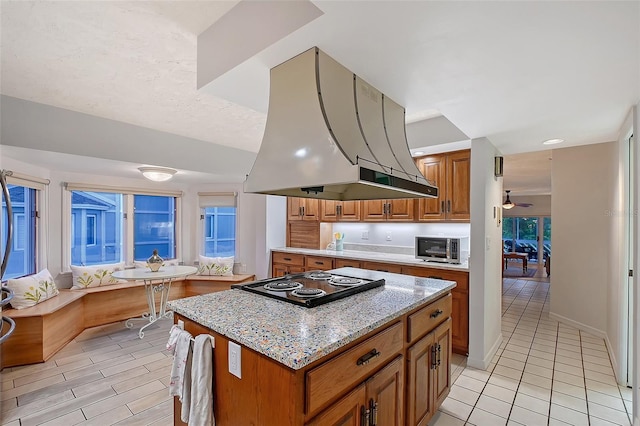 kitchen with island range hood, stovetop, brown cabinets, stainless steel microwave, and a center island