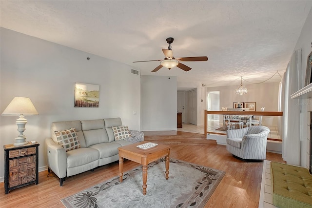 living room with a ceiling fan, a chandelier, light wood finished floors, and baseboards