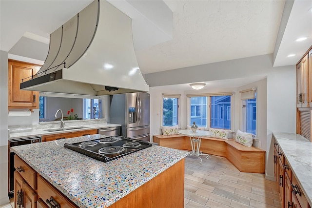 kitchen with exhaust hood, appliances with stainless steel finishes, a kitchen island, a sink, and light stone countertops