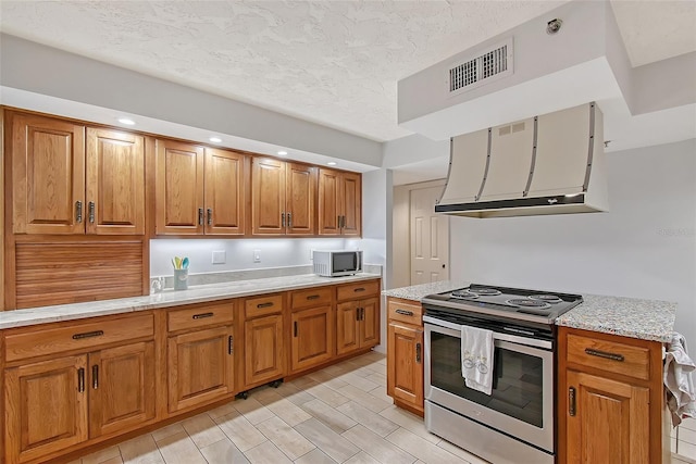 kitchen featuring stainless steel appliances, ventilation hood, brown cabinetry, a textured ceiling, and recessed lighting