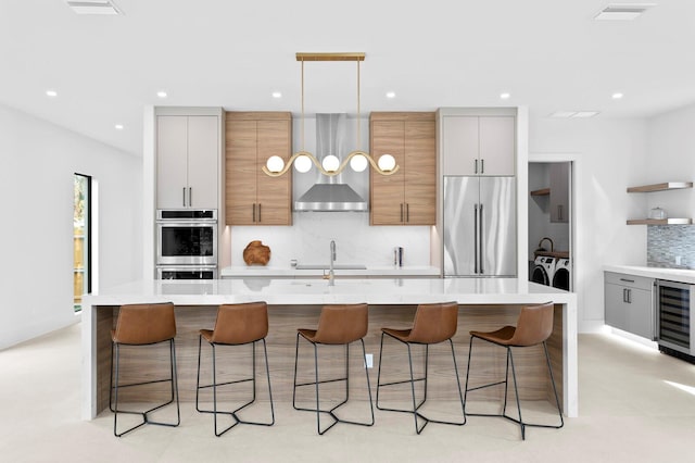 2554 Arlington St, Sarasota, FL 34239 - kitchen featuring washing machine and dryer, beverage cooler, wall chimney exhaust hood, appliances with stainless steel finishes, and backsplash