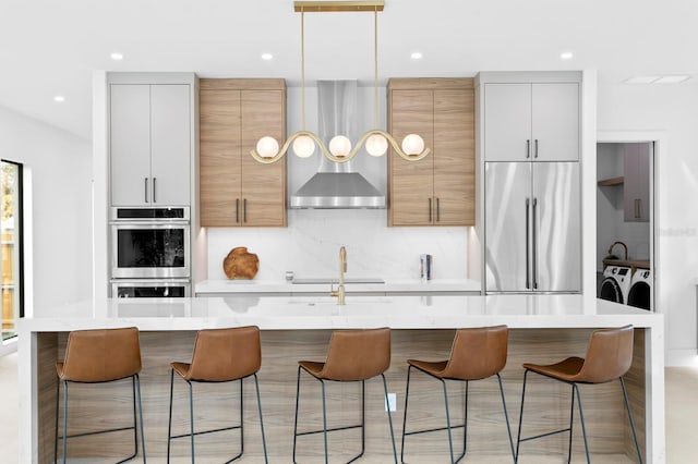 2554 Arlington St, Sarasota, FL 34239 - kitchen with washing machine and dryer, wall chimney range hood, light countertops, appliances with stainless steel finishes, and backsplash