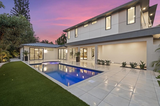 1559 Bay Rd, Sarasota, FL 34239 - back of property at dusk with a jacuzzi, stucco siding, an outdoor pool, a patio area, and a lawn
