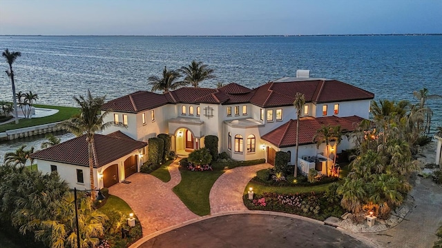 view of front of property featuring a water view, stucco siding, curved driveway, and an attached garage