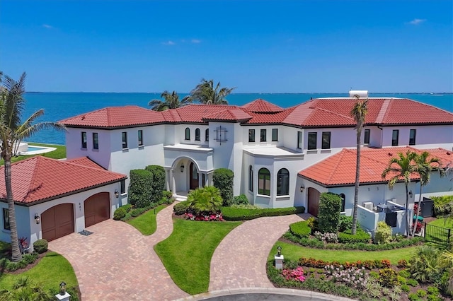 mediterranean / spanish house featuring a water view, stucco siding, an attached garage, and decorative driveway