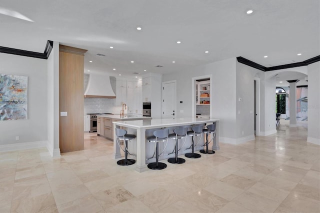 kitchen with a spacious island, stainless steel appliances, decorative columns, light countertops, and premium range hood