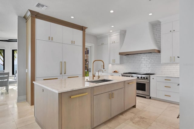 kitchen featuring a sink, visible vents, high end stainless steel range oven, premium range hood, and tasteful backsplash