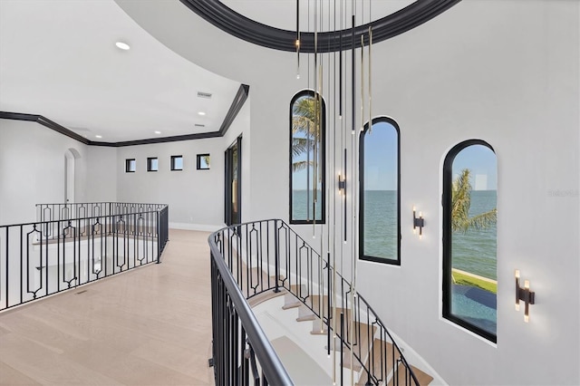 hall with baseboards, ornamental molding, visible vents, a water view, and an upstairs landing