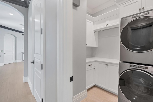 clothes washing area with stacked washing maching and dryer, crown molding, cabinet space, and arched walkways