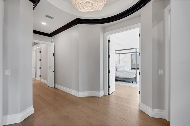 hallway with wood finished floors, ornamental molding, visible vents, an inviting chandelier, and baseboards