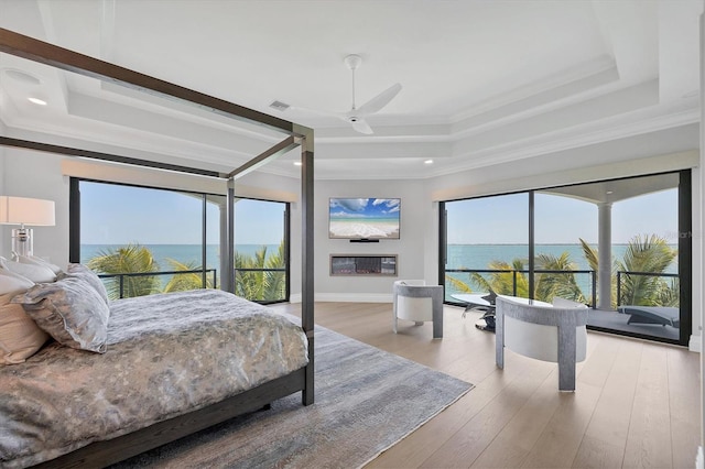 bedroom featuring multiple windows, wood finished floors, a raised ceiling, and ornamental molding