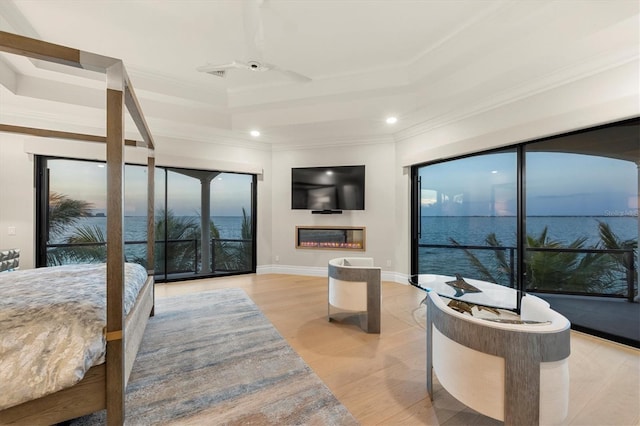 bedroom featuring wood finished floors, a tray ceiling, a glass covered fireplace, ornamental molding, and recessed lighting