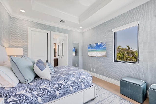 bedroom with wood finished floors, ornamental molding, visible vents, a tray ceiling, and connected bathroom