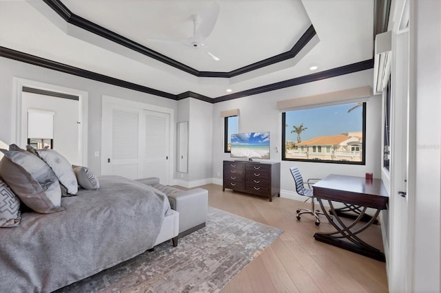 bedroom featuring a closet, ornamental molding, recessed lighting, a tray ceiling, and light wood-style floors