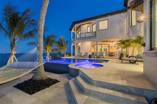 pool at twilight with an in ground hot tub, a patio area, outdoor dining area, and an infinity pool