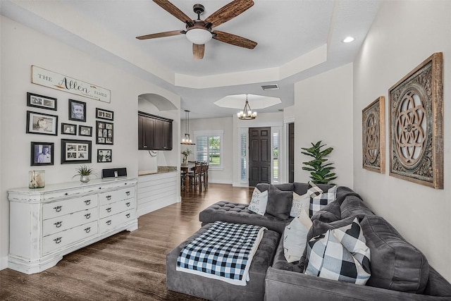 living room with visible vents, dark wood-type flooring, a tray ceiling, arched walkways, and ceiling fan with notable chandelier