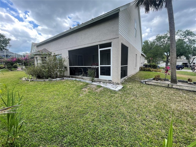 rear view of property with a sunroom, stucco siding, and a yard