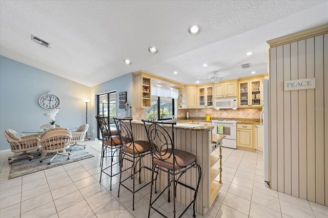 kitchen featuring white appliances, a kitchen breakfast bar, light tile patterned floors, a peninsula, and a textured ceiling