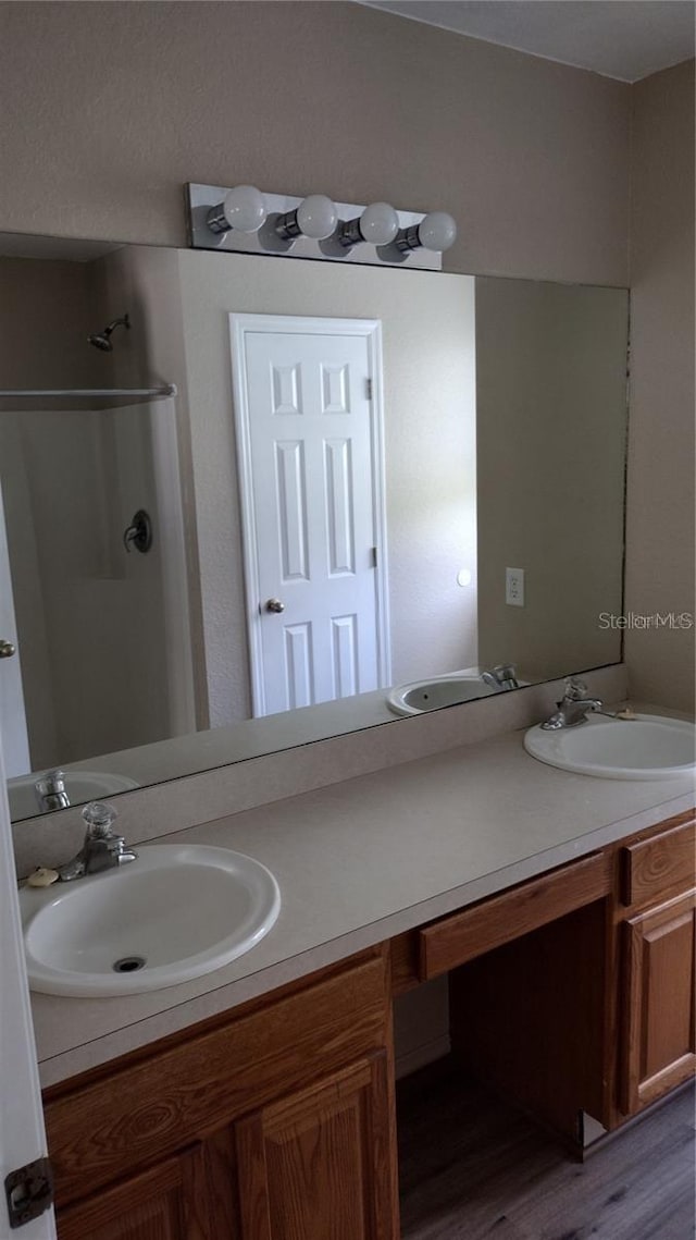 full bathroom with double vanity, wood finished floors, a walk in shower, and a sink
