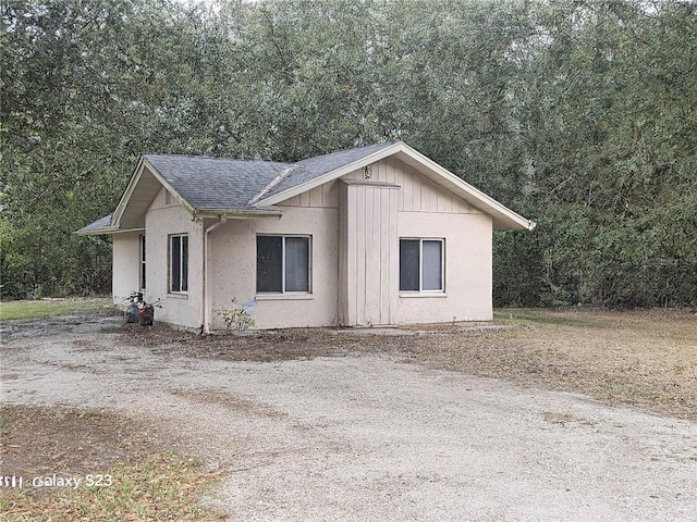 view of home's exterior with driveway, a wooded view, stucco siding, and roof with shingles