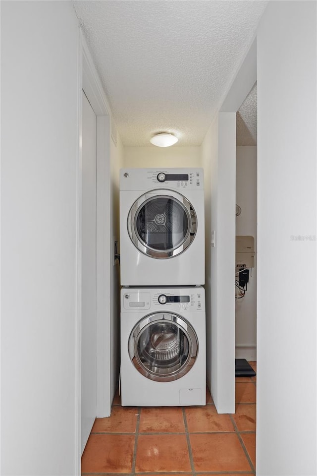 laundry area with tile patterned floors, stacked washer and clothes dryer, a textured ceiling, and laundry area