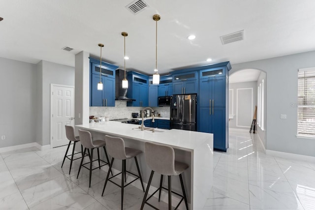 kitchen with blue cabinetry, visible vents, stainless steel fridge with ice dispenser, marble finish floor, and wall chimney exhaust hood
