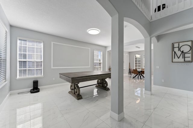 recreation room with baseboards, arched walkways, and marble finish floor