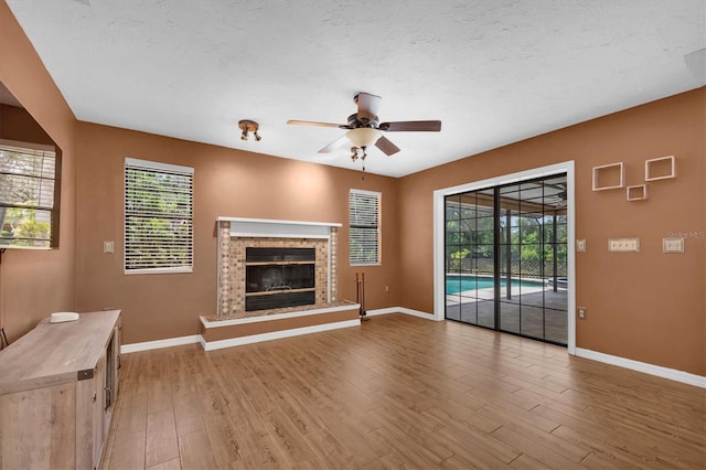 unfurnished living room featuring baseboards, ceiling fan, a brick fireplace, and wood finished floors