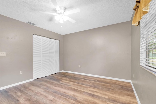 unfurnished bedroom featuring visible vents, a closet, wood finished floors, baseboards, and a textured ceiling