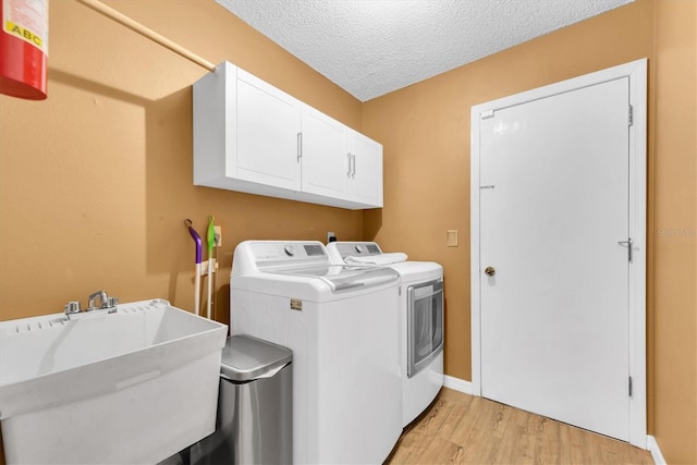 laundry area featuring a textured ceiling, light wood-type flooring, cabinet space, a sink, and washer and dryer