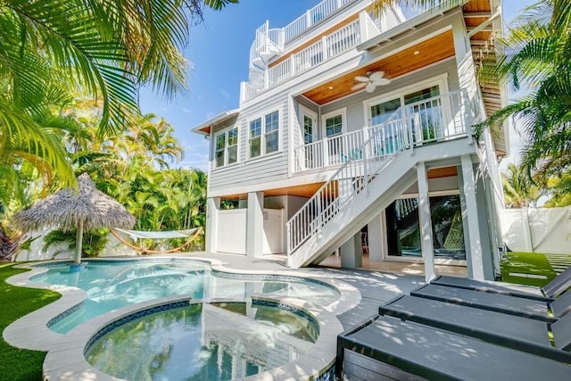 rear view of house with stairs, a balcony, ceiling fan, fence, and a pool with connected hot tub