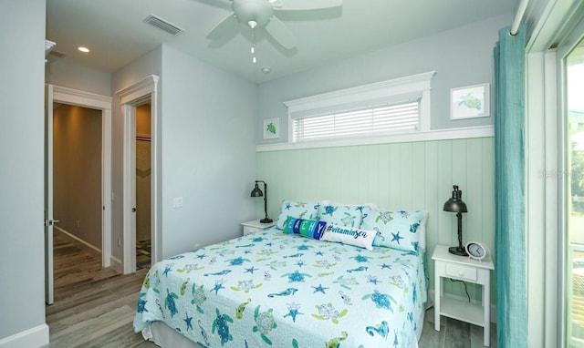 bedroom featuring wood finished floors, wainscoting, and ceiling fan