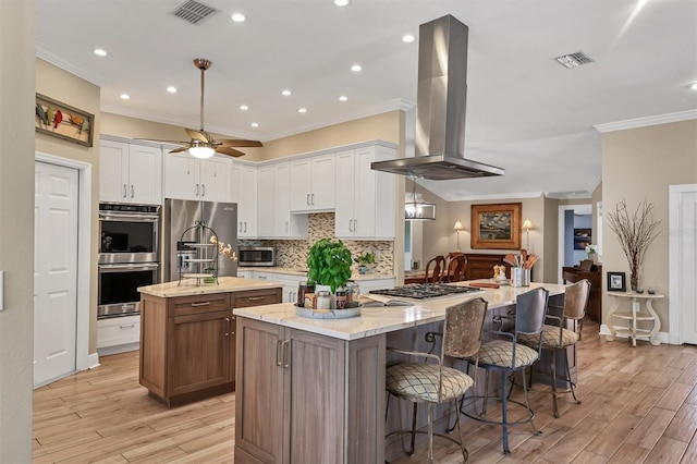 kitchen featuring visible vents, ornamental molding, island range hood, a spacious island, and appliances with stainless steel finishes
