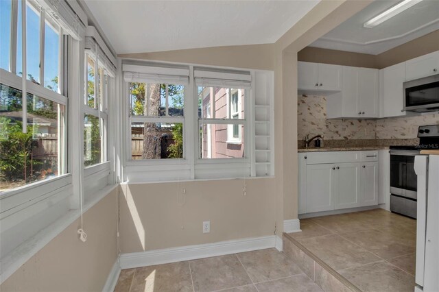 1830 Virginia Dr, Bradenton, FL 34205 - kitchen featuring light tile patterned floors, stainless steel appliances, white cabinets, decorative backsplash, and lofted ceiling