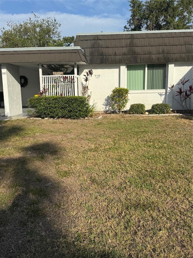 view of side of home featuring a lawn, stucco siding, and mansard roof