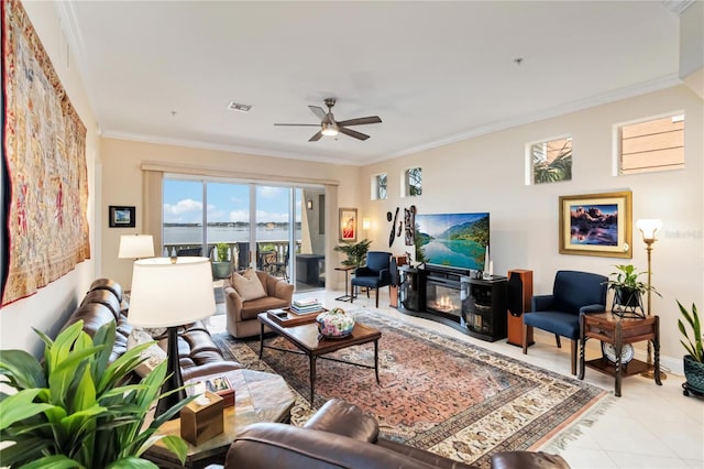 tiled living room featuring crown molding, a ceiling fan, baseboards, and a glass covered fireplace