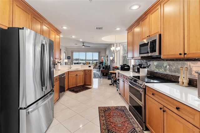 kitchen featuring appliances with stainless steel finishes, a peninsula, backsplash, light countertops, and a sink