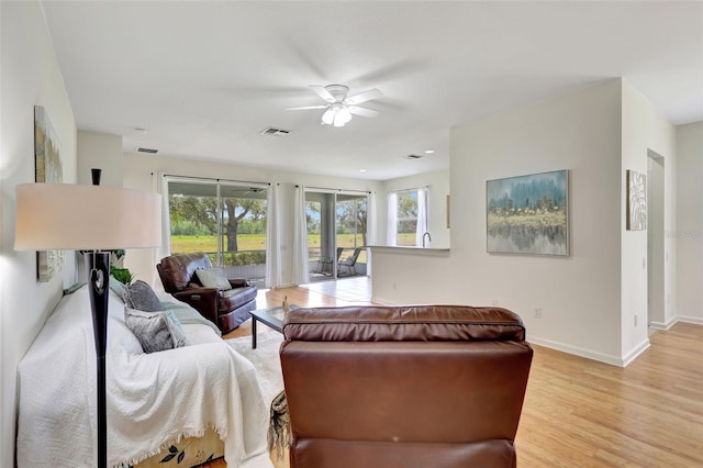 living area featuring baseboards, light wood finished floors, ceiling fan, and a wealth of natural light