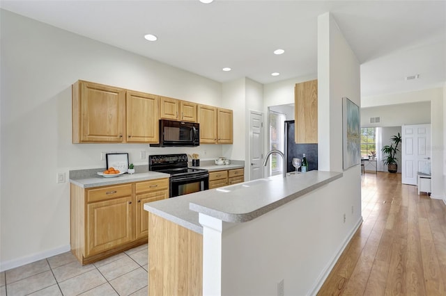 kitchen featuring a sink, light countertops, a peninsula, baseboards, and black appliances