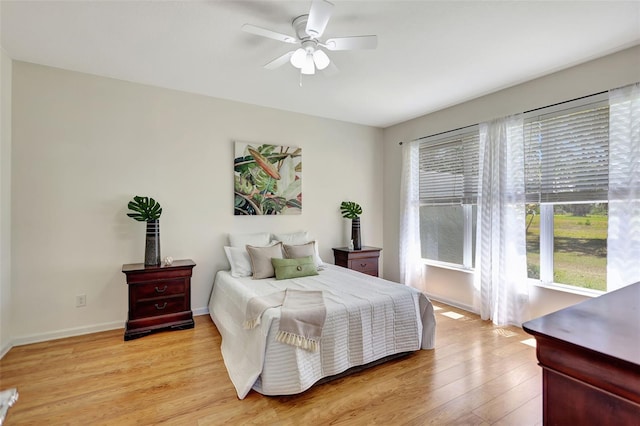 bedroom with baseboards, ceiling fan, multiple windows, and light wood-style flooring