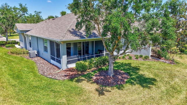 exterior space with a lawn, a shingled roof, a sunroom, and cooling unit