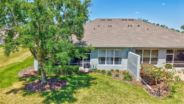 rear view of property with a yard, a shingled roof, a sunroom, and stucco siding
