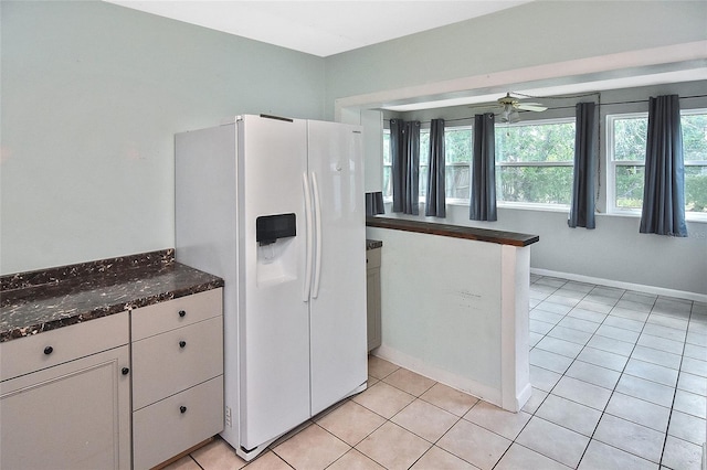 kitchen featuring a ceiling fan, white refrigerator with ice dispenser, light tile patterned floors, dark stone counters, and white cabinetry