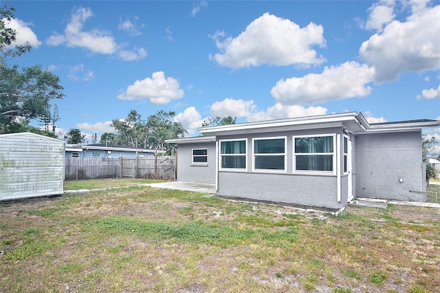 rear view of property with a lawn, fence, and stucco siding