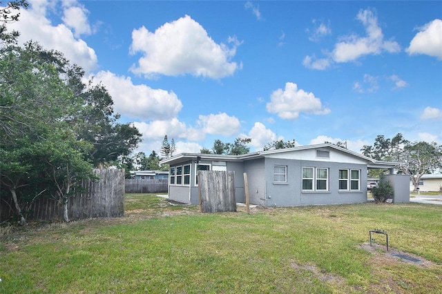 rear view of house featuring a yard, fence, and stucco siding