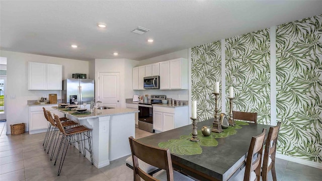 kitchen featuring appliances with stainless steel finishes, white cabinetry, wallpapered walls, visible vents, and a center island with sink