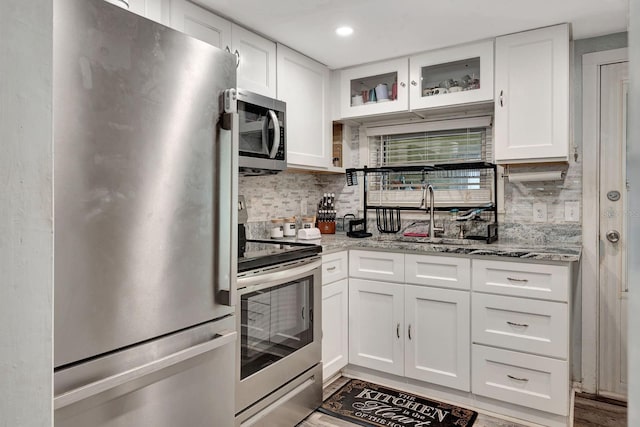 kitchen featuring light stone countertops, appliances with stainless steel finishes, a sink, white cabinetry, and tasteful backsplash