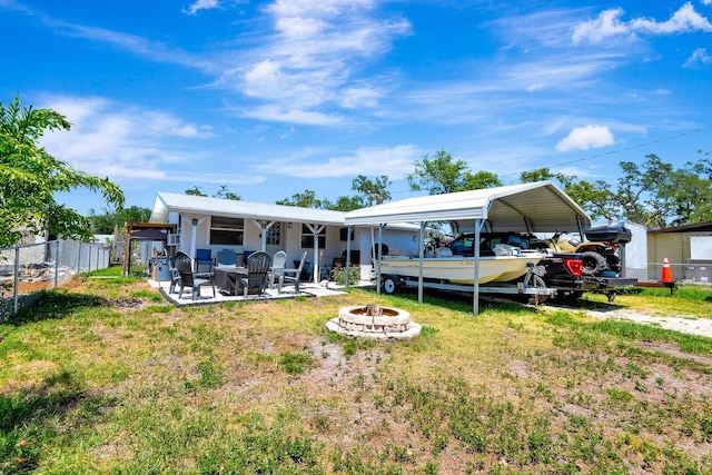back of house with fence, a detached carport, a lawn, and a fire pit