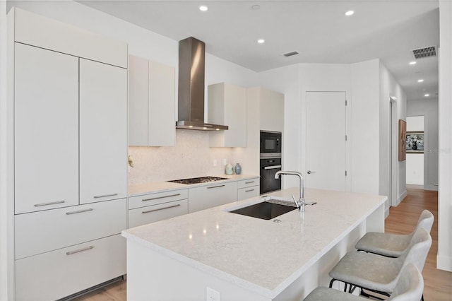 kitchen featuring wall chimney exhaust hood, a sink, black appliances, light wood finished floors, and recessed lighting